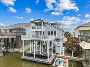 A waterfront property with a covered dock, a small boat, and a lush garden. - Three C`s- Canal front / short walk to beach (Galveston)