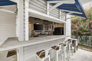 An outdoor kitchen area with a bar counter, seating, and a view of the interior. - Three C`s- Canal front / short walk to beach (Galveston)