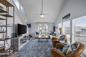 A spacious living room with a flat-screen TV, a fireplace, a large window, and a ceiling fan. - Three C`s- Canal front / short walk to beach (Galveston)