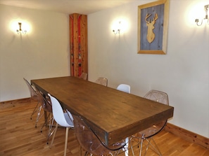Une salle de conférence avec une longue table en bois, des chaises en plastique transparent et des luminaires fixés au mur.