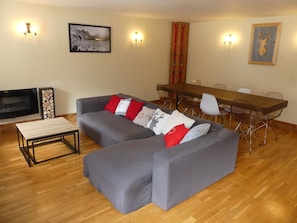 A living room with a grey sofa, a wooden coffee table, a TV, and a dining area with a wooden table and chairs. - Charming apartment - 7 guests (Pralognan-la-Vanoise)