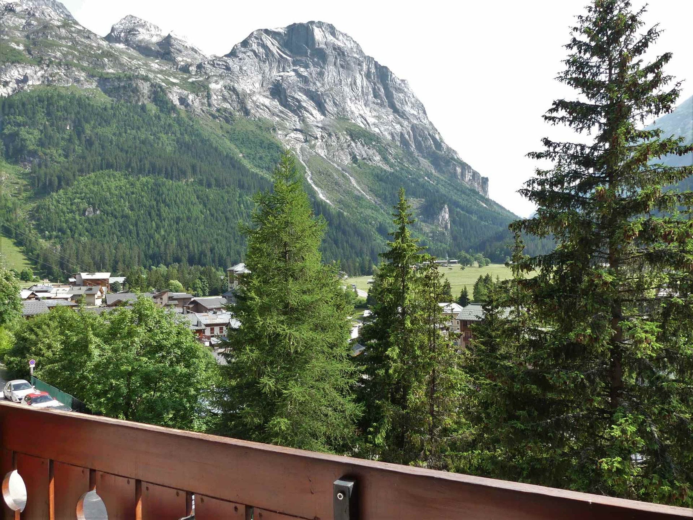 A mountain landscape with a village in the valley, a wooden deck, and a view of the mountains.