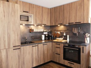 A modern kitchen with wooden cabinets, a microwave, a coffee machine, and various utensils. - Cozy apartment, balcony - 4 guests (Pralognan-la-Vanoise)