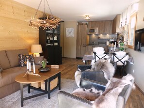 A modern living room with a sofa, a coffee table, and a fireplace. There is a kitchen in the background with wooden cabinets and a microwave. - Cozy apartment, balcony - 4 guests (Pralognan-la-Vanoise)