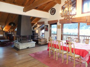 A dining area with a table set for six, wooden chairs, and a view of a snowy landscape through large windows. - Spacious apartment with balcony - 8 guests (Pralognan-la-Vanoise)