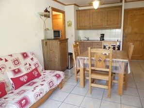 Ein gemütlicher, kompakter Wohnbereich mit Sofa, Esstisch, Stühlen, einer Mikrowelle und Holzschränken.