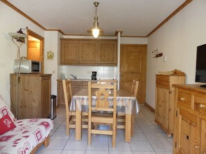 Eine kompakte Küche mit Holzschränken, einem Esstisch mit Stühlen, einer Mikrowelle und einem Fernseher auf einem Holzkasten.