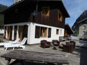 Eine Chalet mit einer Terrasse, Liegestühlen und einem Grillplatz.