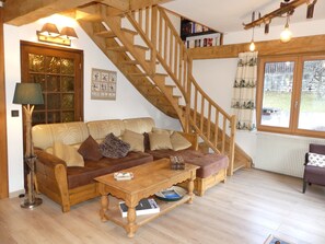 Ein gemütliches Wohnzimmer mit einer Holztreppe, einer Sofagarnitur, einem Couchtisch und einem Bücherregal.