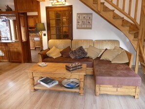 Ein gemütliches Wohnzimmer mit einer Holztreppe, einer Sofagarnitur und einem Couchtisch mit Büchern und einer Zeitschrift.