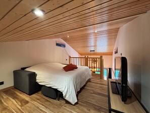 Ein Schlafzimmer mit Bett, einer kleinen Sitzecke, einem Fernseher und Blick ins Freie.