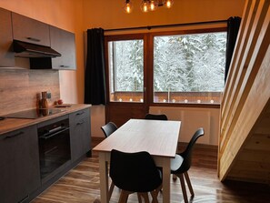 Cozinha moderna com área de refeições, piso de madeira e uma grande janela com vista para árvores cobertas de neve.