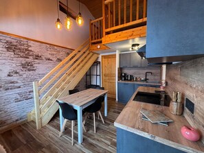 Cozinha moderna com ilha de madeira, área de jantar com mesa e cadeiras, e escada que leva a um andar superior.
