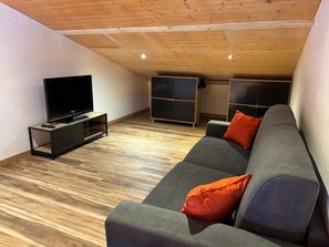 Uma sala de estar moderna com uma TV de tela plana, um sofá cinza com almofadas laranja e armários embutidos.