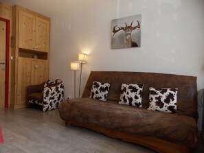 Ein gemütliches Zimmer mit einem braunen Sofa, Kissen mit Kuhmuster, einem Holzschrank und einem Bild von einem Reh.