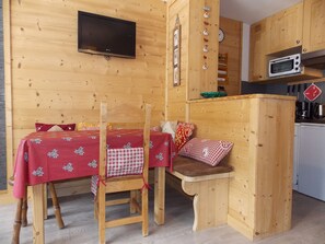 Ein Interieur einer Holzhütte mit Esstisch, Stühlen, Fernseher und Küchenzeile.
