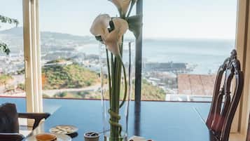 A dining table with various breakfast items and a vase of flowers, overlooking a scenic view.