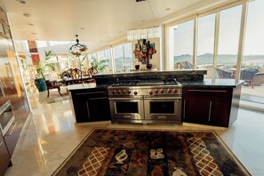 A modern kitchen with a large island, stainless steel appliances, and a view of the city. - Pedregal Villa with 75-ft Infiniti Pool + Panoramic Views (Cabo San Lucas)