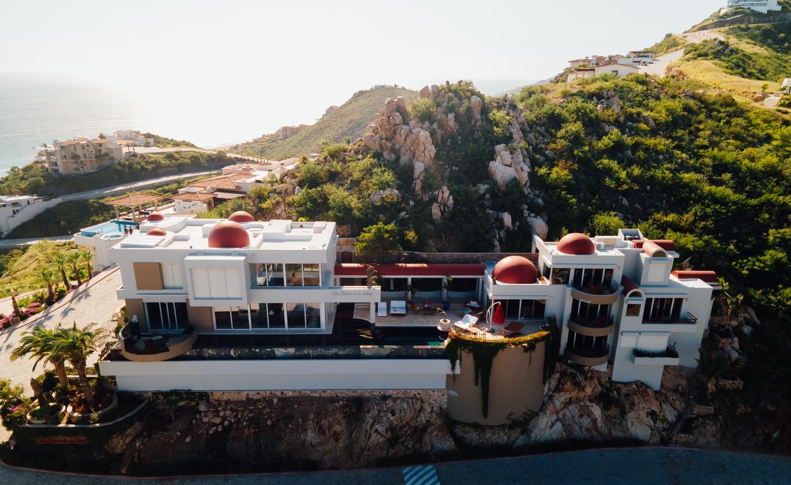 A modern hotel with multiple buildings, a pool, and a view of the sea.