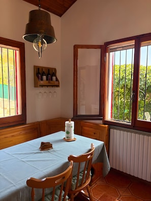 Ein Essbereich mit einem Tisch für zwei Personen, Holzstühlen, einer hängenden Leuchte und einem Fenster mit Blick auf Grünflächen.