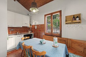A kitchen with white cabinets, a dining table with chairs, a hanging light fixture, and a window with a view of greenery.