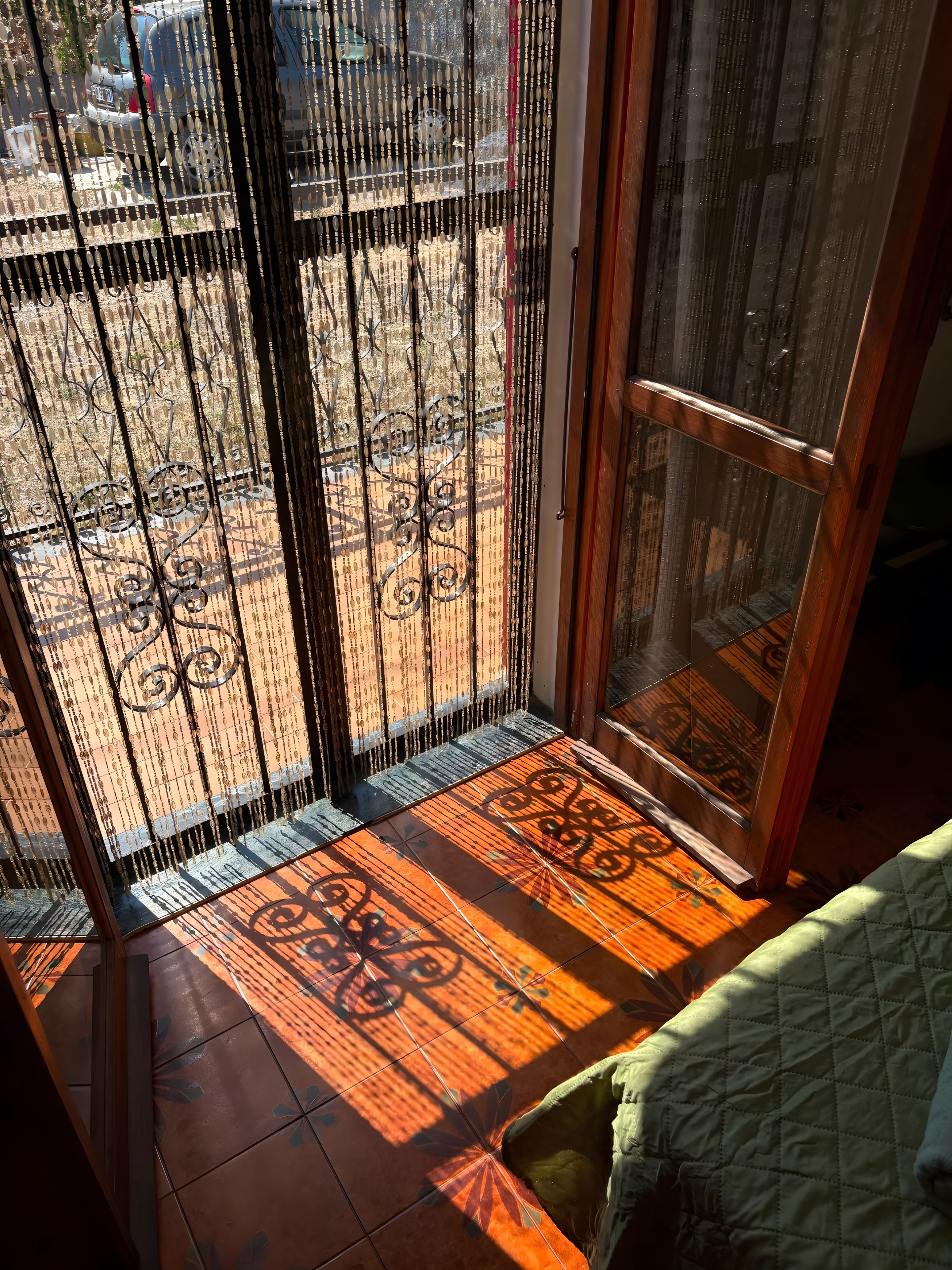 A room with a sliding glass door leading to an outdoor area, a patterned floor, and a green cushion.