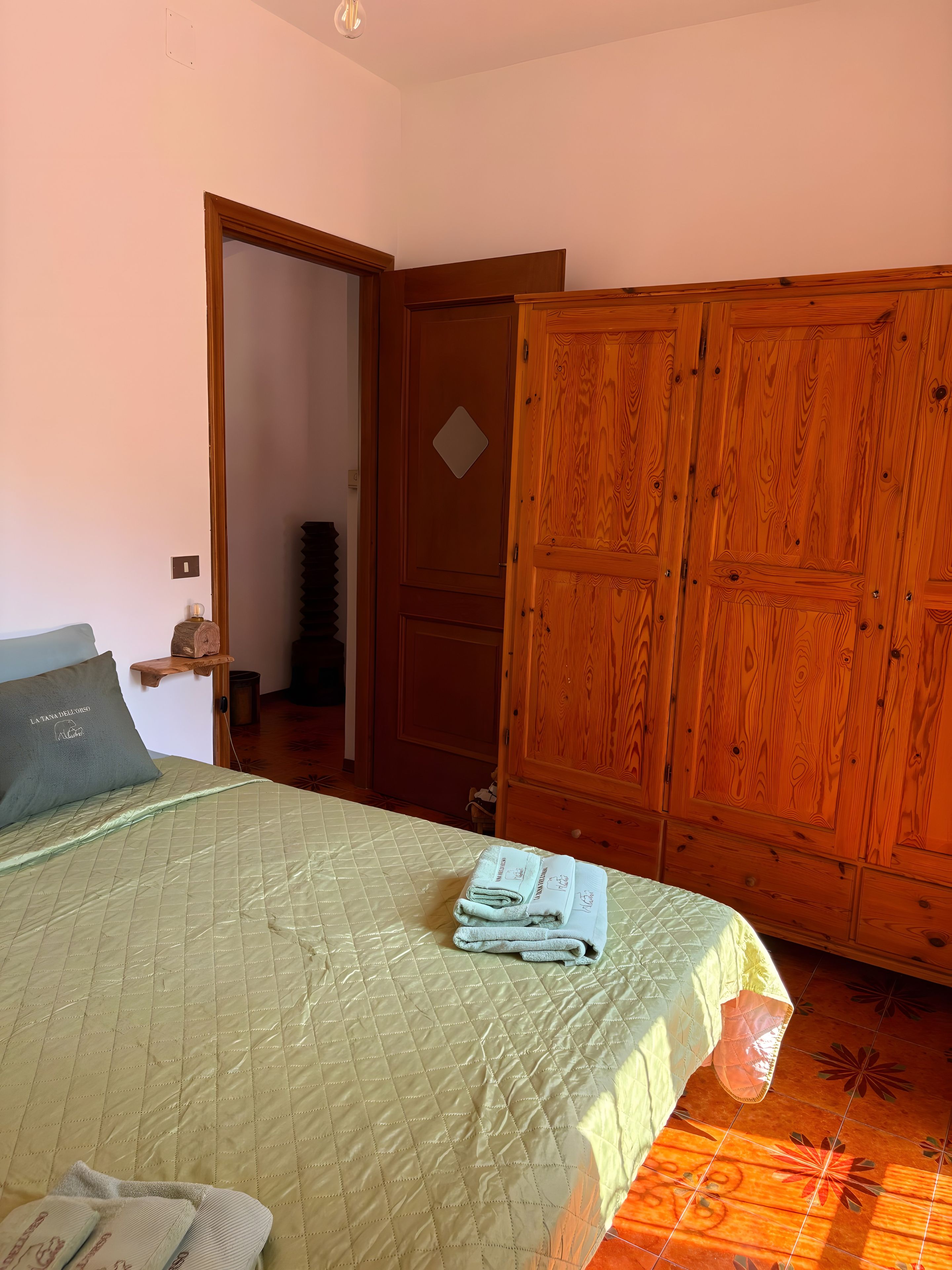 Un dormitorio con cama, un armario de madera y una puerta que da a otra habitación.