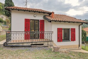 A two-story house with a balcony, red shutters, and a tiled roof.
