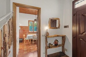 A hallway with a wooden door, a rustic shelf with decorative items, and a dining area with a table and chairs.