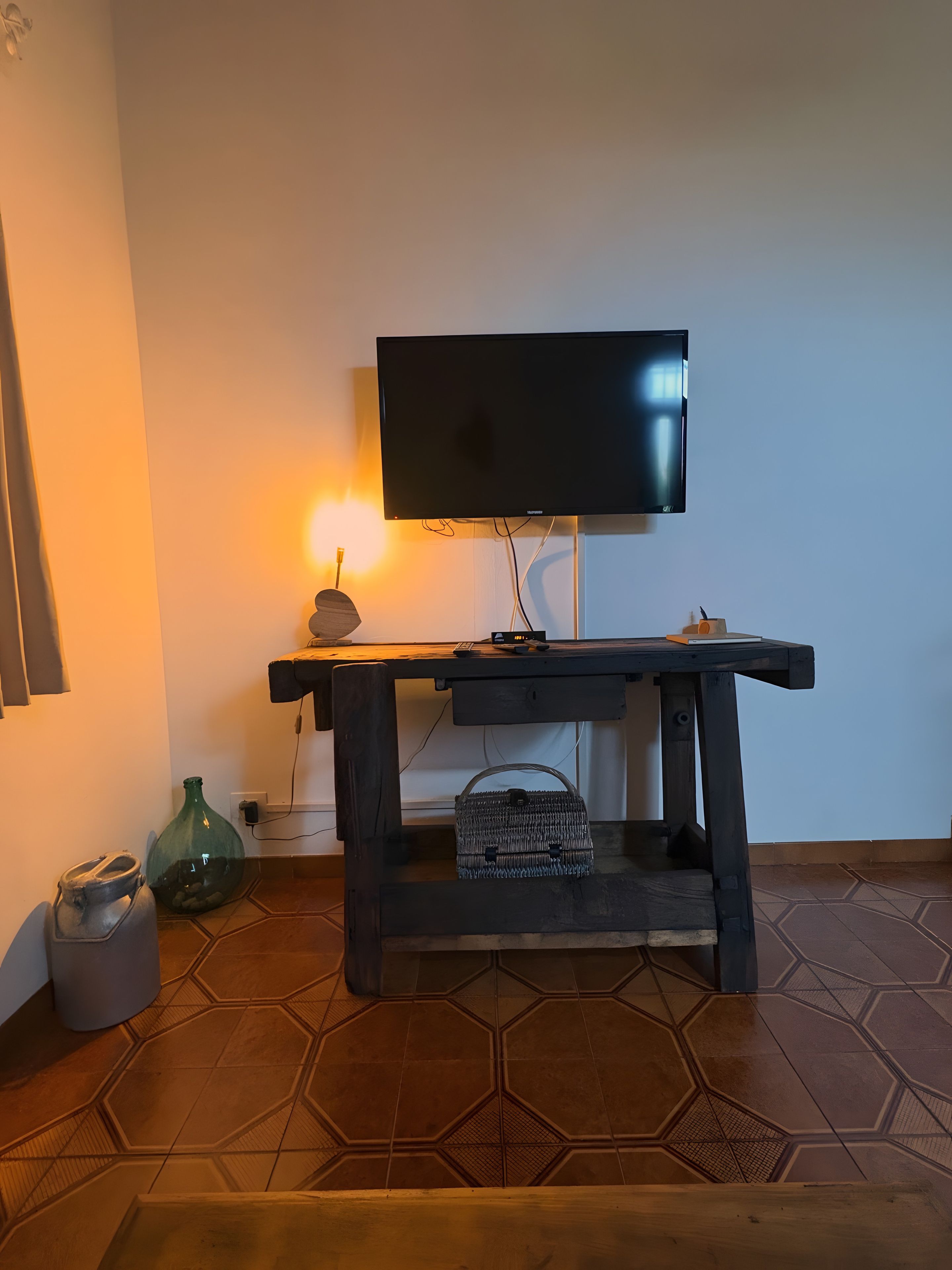 Ein Zimmer mit an der Wand befestigtem Fernseher, einem Holztisch mit Korb darunter und einem sechseckig gemusterten Boden.