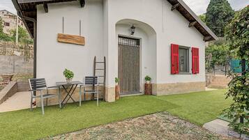 A house with a white exterior, a wooden bench, two chairs, a small table, and a well-maintained lawn.