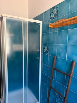 Ein Badezimmer mit Duschkabine aus Glas, blauen Fliesenwänden und einer Holzleiter.