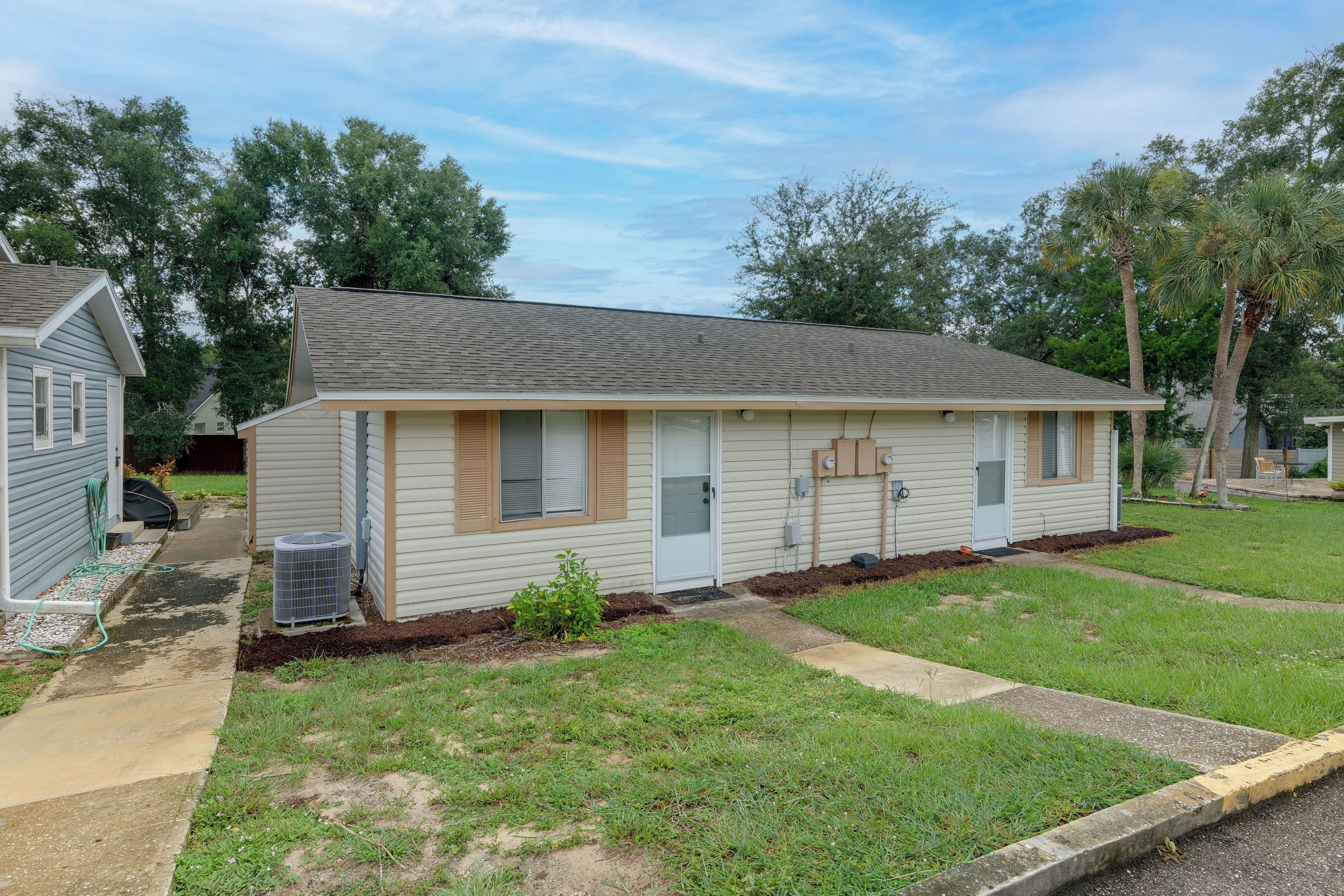 A single-story mobile home with a front porch, a small garden area, and a clear sky.