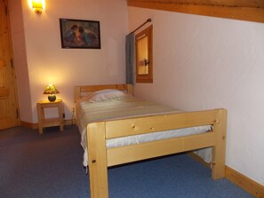 A bedroom with a wooden bed, a bedside table with a lamp, a painting on the wall, and a window with a curtain. - Cozy duplex close to all - 4/6 guests (Pralognan-la-Vanoise)