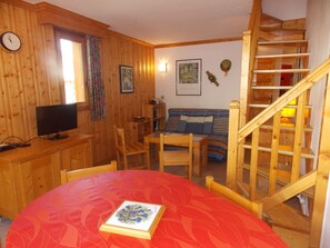 A wooden interior with a dining table, chairs, a television, a sofa, a staircase, and a clock. - Cozy duplex close to all - 4/6 guests (Pralognan-la-Vanoise)