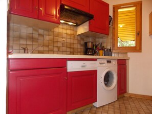 Cuina petita amb armaris vermells, forn integrat, cafetera i rentadora.