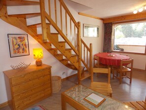 A wooden staircase leading to a dining area with a red tablecloth, a lamp on a wooden cabinet, and a framed picture on the wall. - Cozy duplex close to all - 4/6 guests (Pralognan-la-Vanoise)