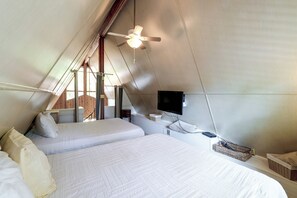 Een kamer met een schuine kap, een bed, een televisie en een plafondventilator.