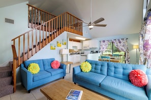Ein Wohnzimmer mit blauen Sofas, einem Holztisch, einer Treppe und einem Küchenbereich.