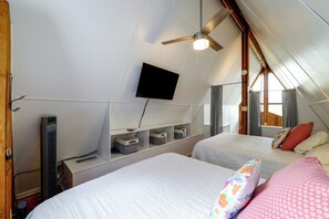 Une chambre avec deux lits, un ventilateur de plafond, un téléviseur fixé au mur et des bacs de rangement.