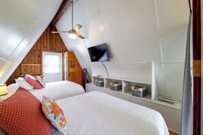 A bedroom with a sloped ceiling, a bed with white bedding, a ceiling fan, a mounted TV, and built-in storage shelves. - Lake Breeze Bungalow: 3 Mi to State Park! (Clermont)