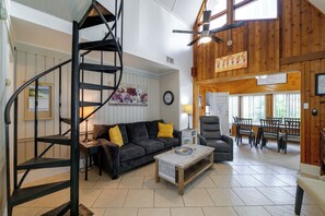 A spacious living area with a black spiral staircase, a dark sofa with yellow cushions, a wooden coffee table, and a dining area with wooden chairs and a table. - Lake Breeze Bungalow: 3 Mi to State Park! (Clermont)