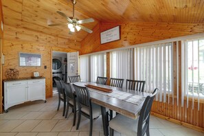 Une pièce aux murs lambrés, comprenant une table à manger, des chaises, un ventilateur de plafond et un coin cuisine équipé d’appareils électroménagers.