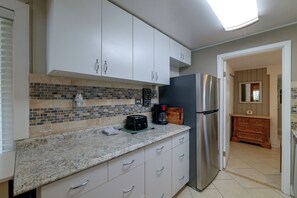 A modern kitchen with white cabinets, a granite countertop, and a stainless steel refrigerator. - Lake Breeze Bungalow: 3 Mi to State Park! (Clermont)