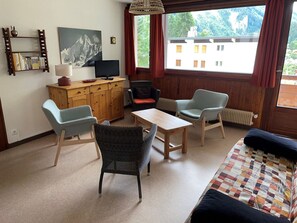 A room with a bed, a wooden table, two chairs, a television on a wooden cabinet, and a window with a view of buildings. - Spacious apartment for families - 6 guests (Pralognan-la-Vanoise)