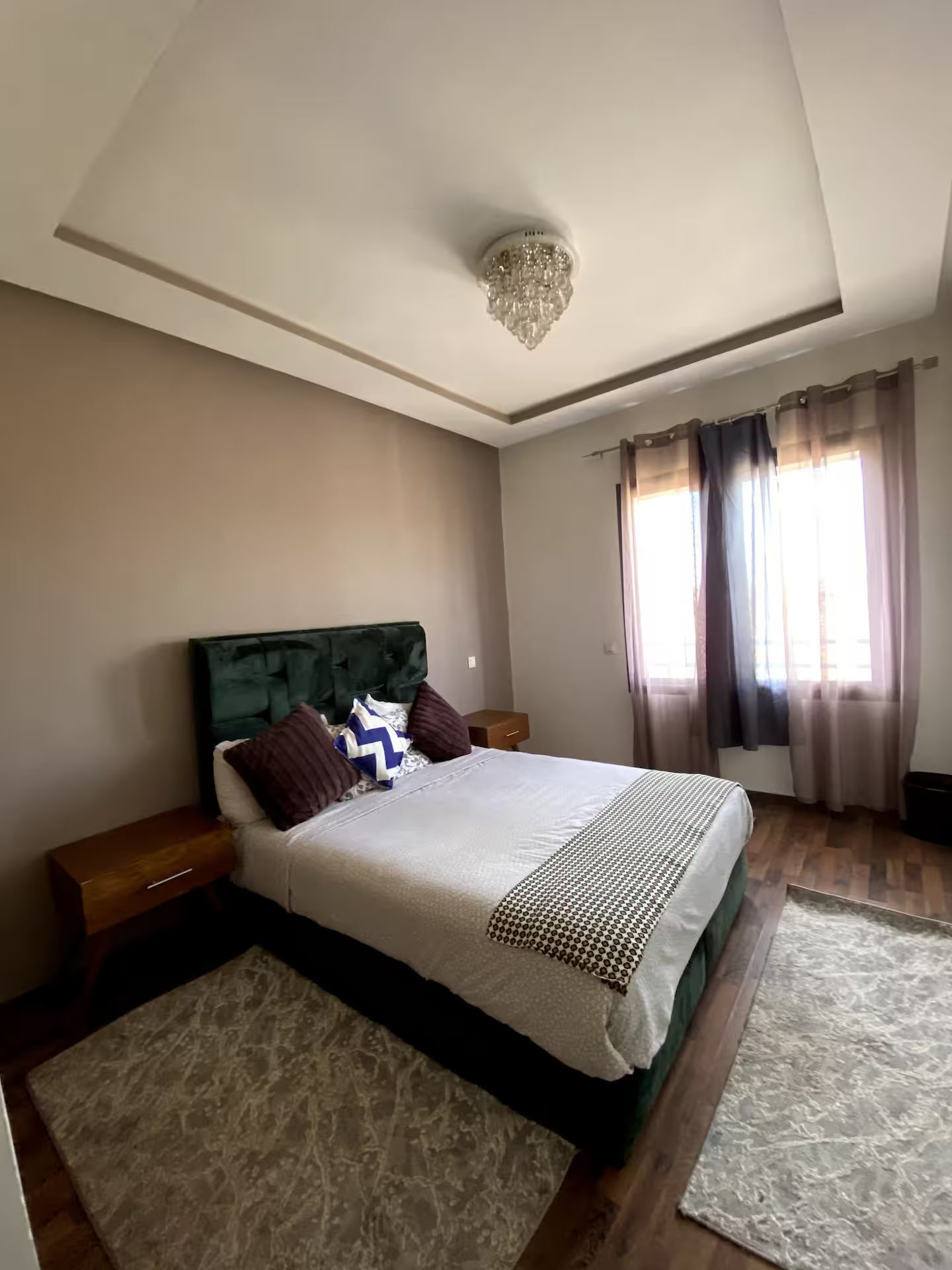 Un dormitorio con cama, mesitas de noche, candelabro, cortinas y suelo de madera.
