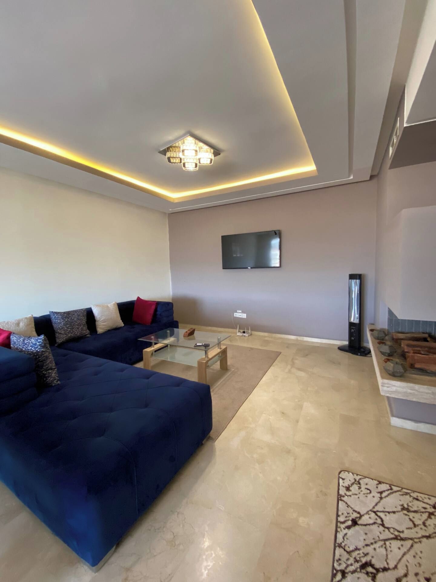 Ein modernes Wohnzimmer mit einem dunkelblauen Sofa, einem Glastisch und einem flachbildfernseher an der Wand.
