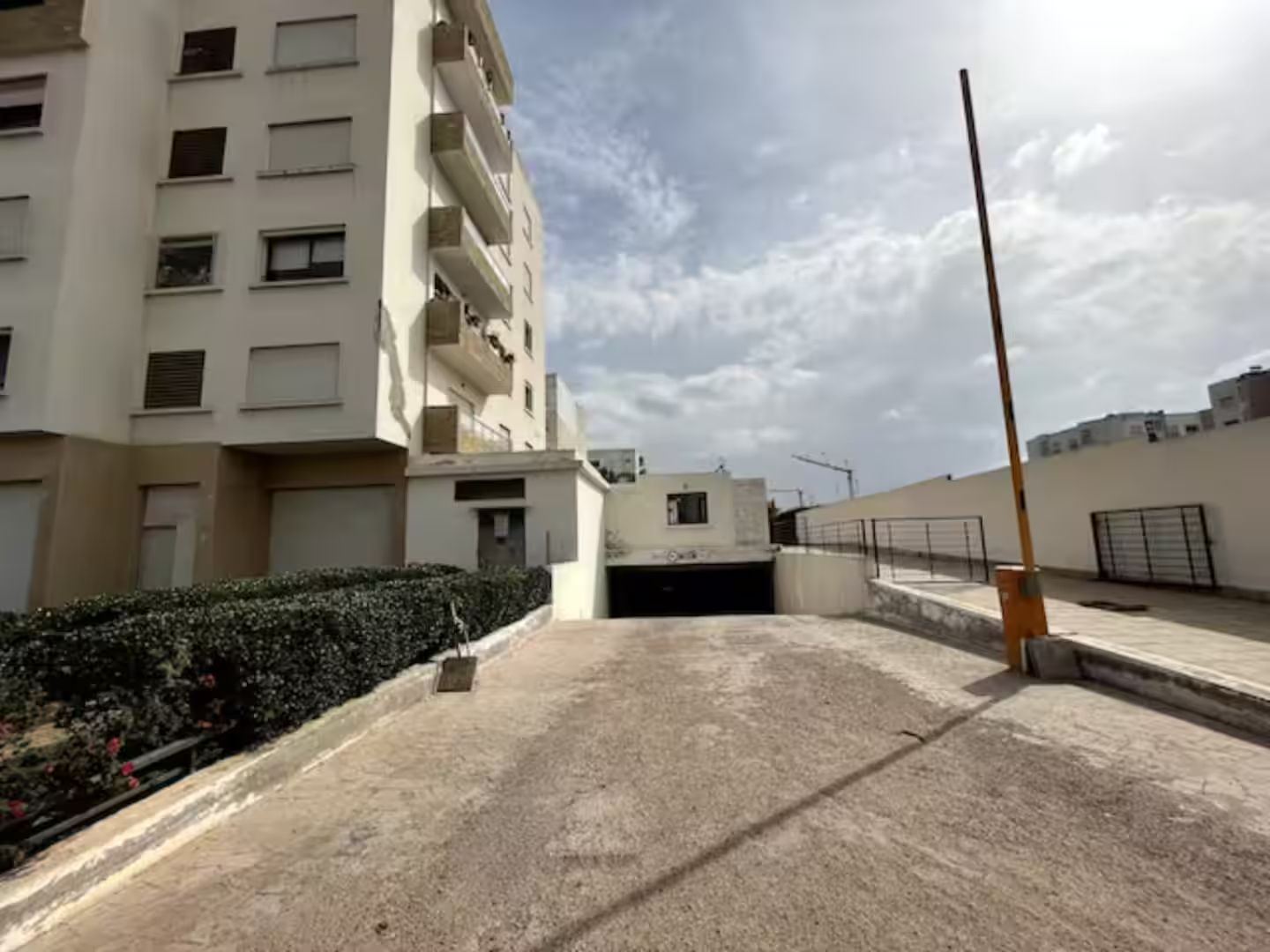 A multi-story residential building with balconies, a gated entrance, and a clear sky.