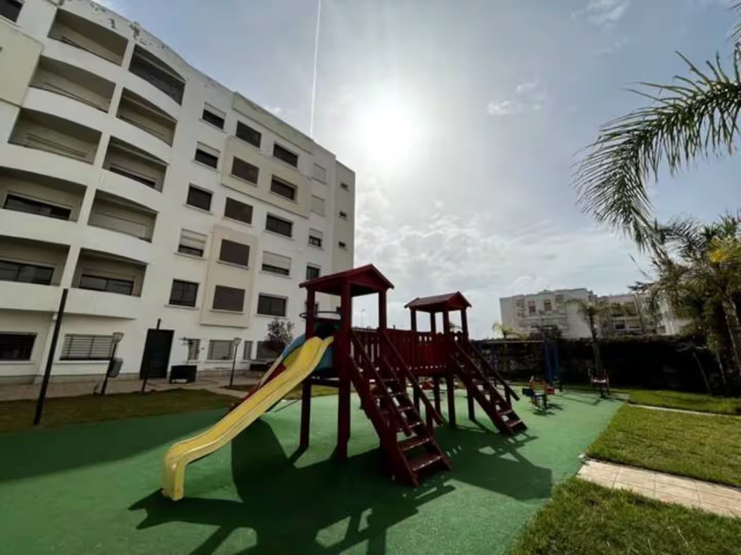 Ein Spielplatz mit Rutsche und Klettergerüsten, umgeben von einem Gebäude mit mehreren Balkonen.