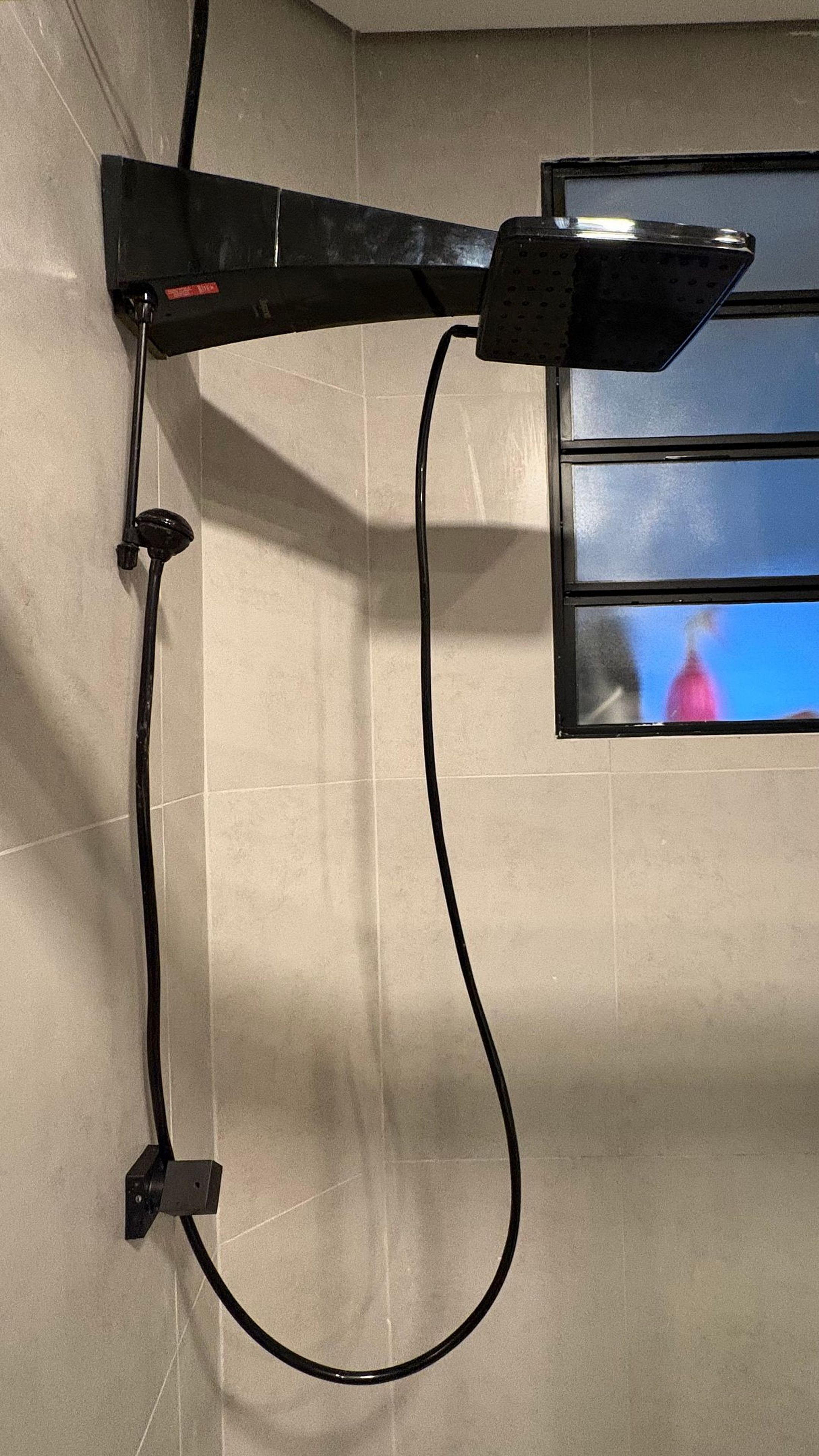 A wall-mounted device with a cable, a window with a view, and a wall with a textured surface.